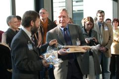 Zwei Männer stehen umringt von weiteren Personen im Foyer des Erwin-Schrödinger-Zentrums. Sie halten Geschenke aus Salzteig und einen Schlüssel in der Hand